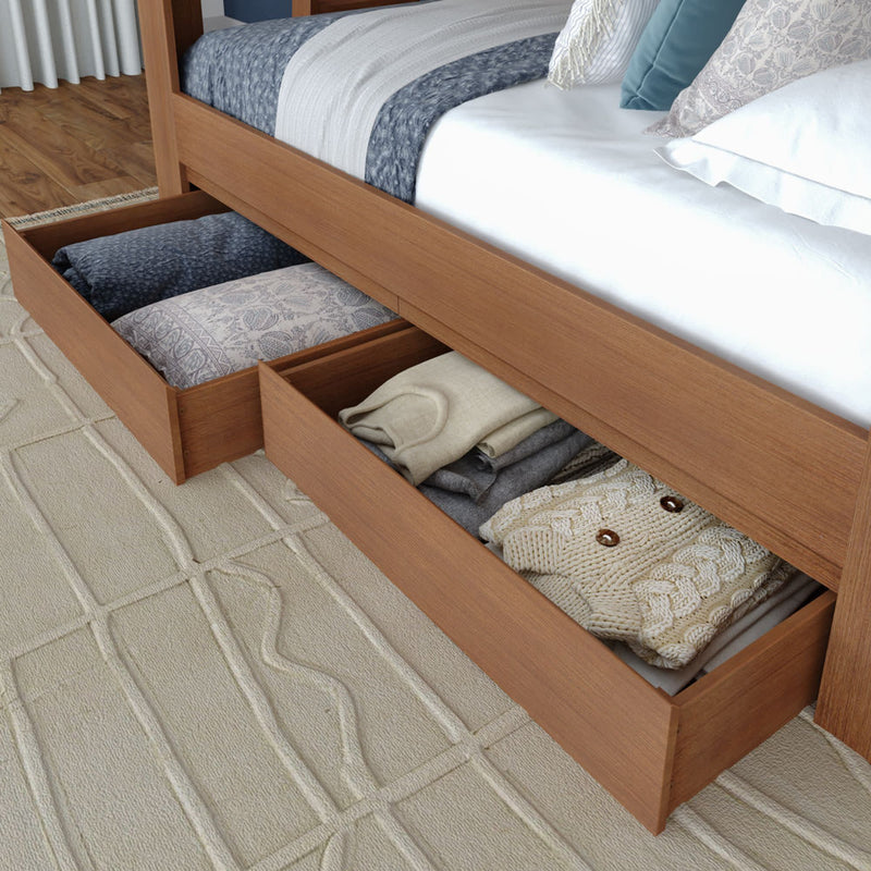 Wooden platform bed with open under-bed storage drawers holding folded sweaters, blankets and pillows — space-saving bedroom storage solution.