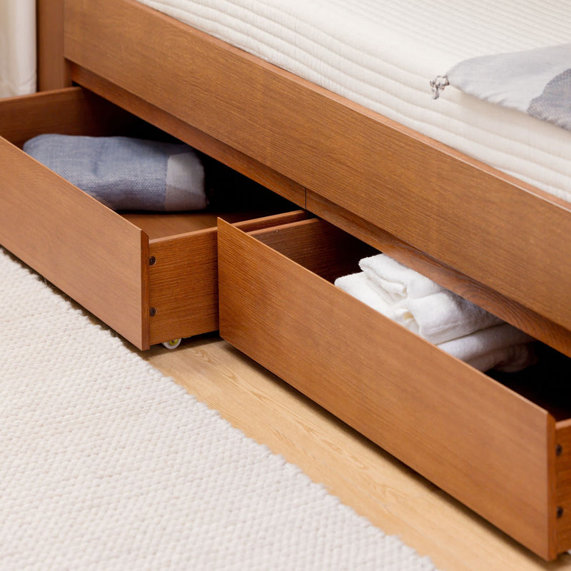 Wooden platform bed with under-bed pull-out drawers storing folded towels and blankets for space-saving bedroom storage