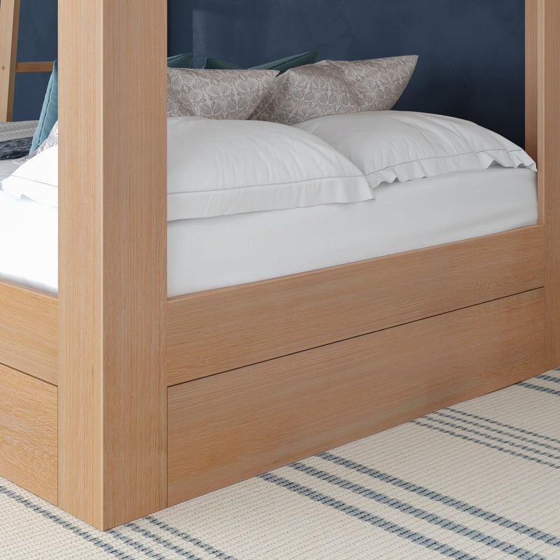 Light oak four-poster platform bed with under-bed storage drawer, crisp white linens and patterned pillows against a navy accent wall over a plaid area rug