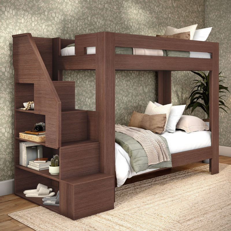 Walnut twin-over-twin wooden bunk bed with built-in staircase shelving, cozy neutral bedding and green floral wallpaper in a space-saving kids' bedroom