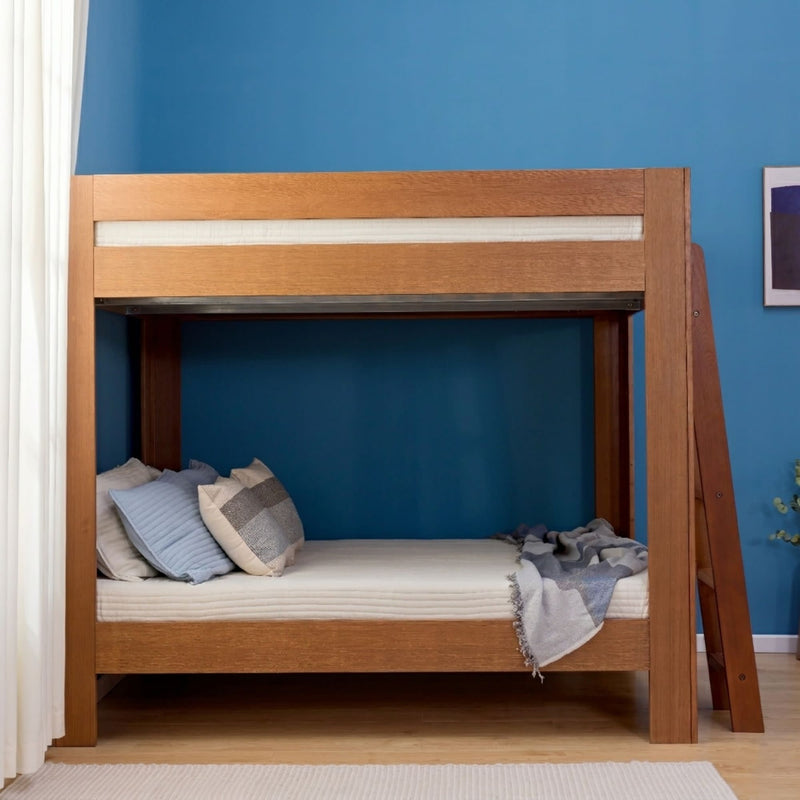 Solid wood bunk bed with ladder, cozy mattress and throw pillows against a blue accent wall, space-saving kids bedroom