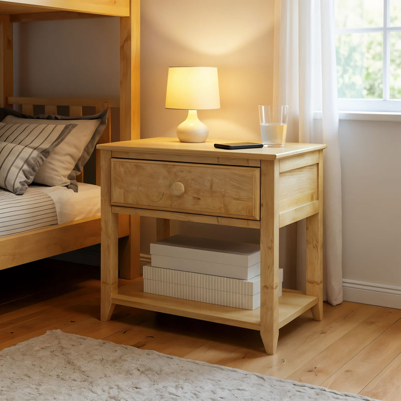 Wooden nightstand with drawer, bedside lamp, and glass of water in cozy bedroom setting.