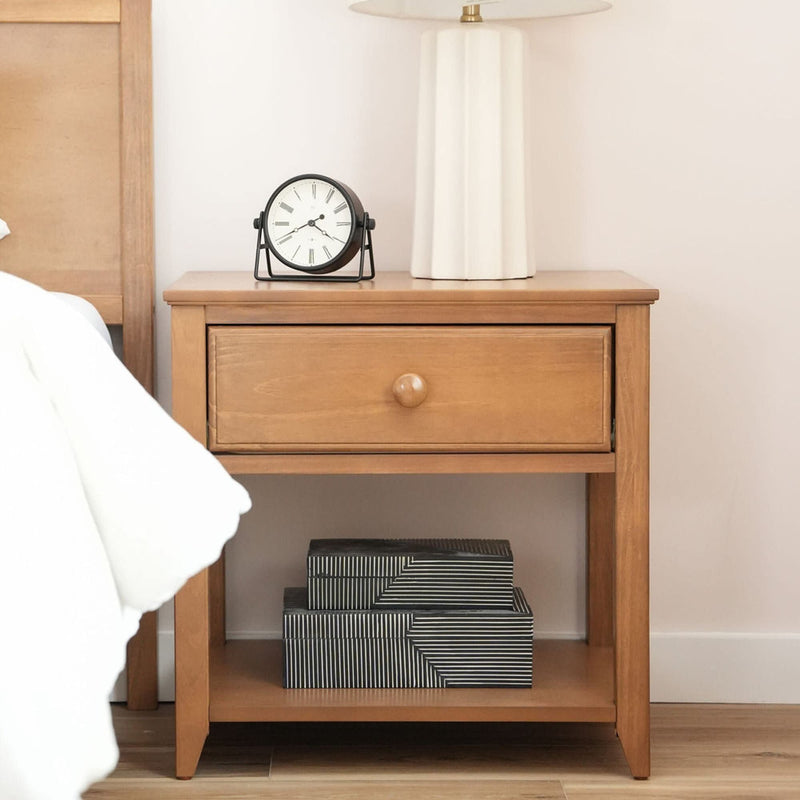 Wooden bedside table with a classic clock, modern lamp, and decorative storage boxes.