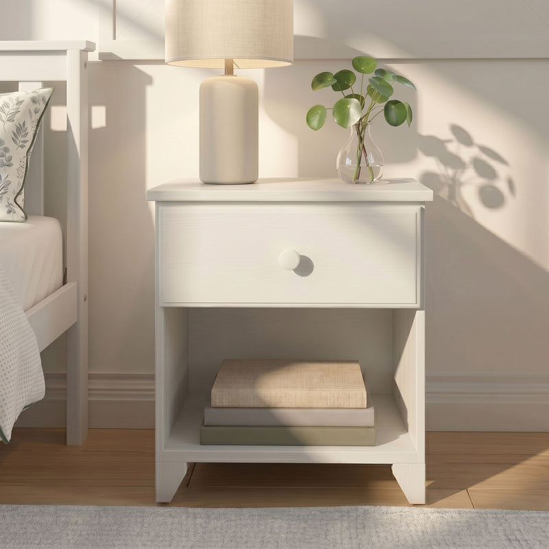 White nightstand with ceramic table lamp and glass vase holding pilea (Chinese money plant) on wooden floor in minimalist neutral bedroom decor