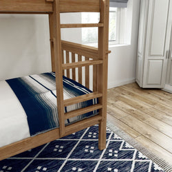 Wooden bunk bed with blue patterned bedding in a cozy bedroom with hardwood floors and a geometric area rug.