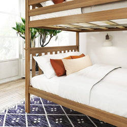 Wooden bunk bed with white bedding and orange pillows, next to a green plant and modern wall lamp in a sunlit room.