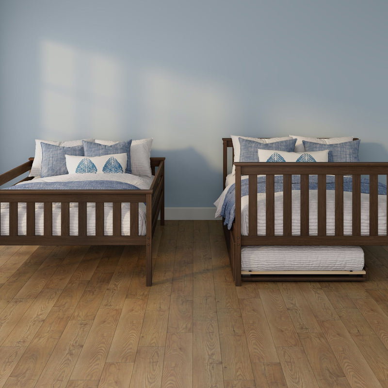 Two wooden twin beds with blue-and-white bedding and decorative pillows in a light blue bedroom with hardwood floors and an under-bed trundle.