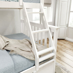 White wooden bunk bed ladder with blue bedding and beige throw blanket in a bright modern bedroom.