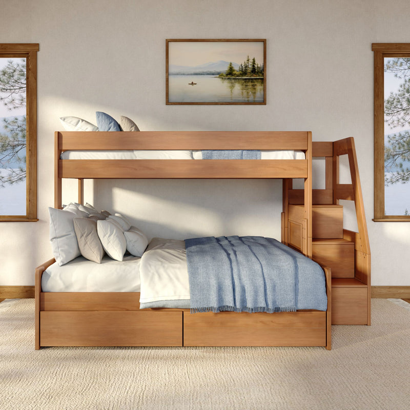 Sunlit modern rustic wooden bunk bed with staircase and built-in storage drawers, layered neutral pillows and blue throw blanket in a cozy bedroom with framed lakeside wall art and large windows.