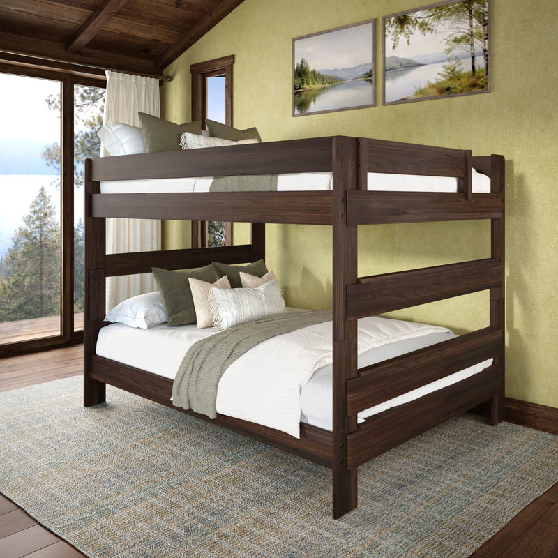 Full-over-full dark walnut solid wood bunk bed in rustic cabin bedroom with green walls, layered neutral bedding and decorative pillows, on a woven rug with lake view through floor-to-ceiling windows