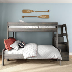 Gray wooden twin-over-full bunk bed with staircase in coastal kids' bedroom, white quilt with red piping, navy and red accent pillows, light blue wall with decorative wooden oars and beige rug on hardwood floor
