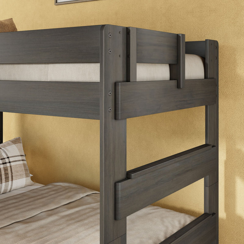 Dark gray wooden bunk bed frame close-up showing guardrails and ladder details against a beige textured wall with neutral bedding and a plaid pillow