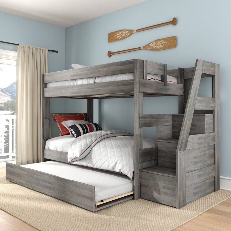 Gray wooden bunk bed with pull-out trundle and stairs in coastal kids bedroom with white quilt, striped pillows and decorative wooden oars on a light blue wall
