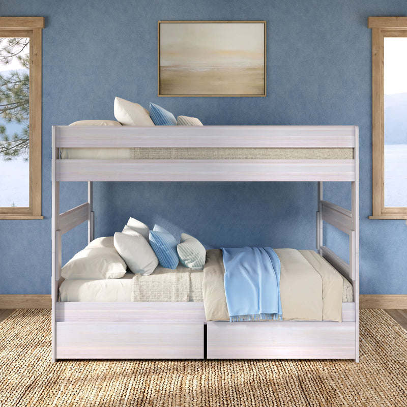 Whitewashed twin-over-full bunk bed with under-bed storage drawers, beige and blue bedding and pillows in a coastal-style blue bedroom with woven rug and lake view
