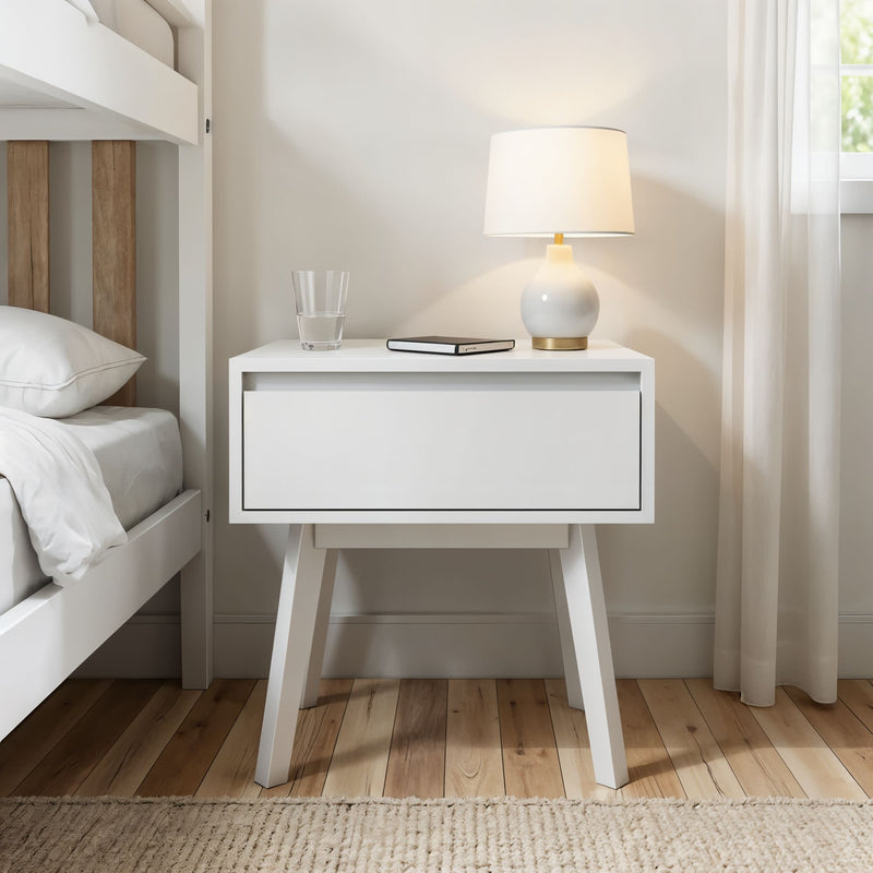 White modern nightstand with a lamp, book, and glass of water beside a bed in a cozy bedroom.
