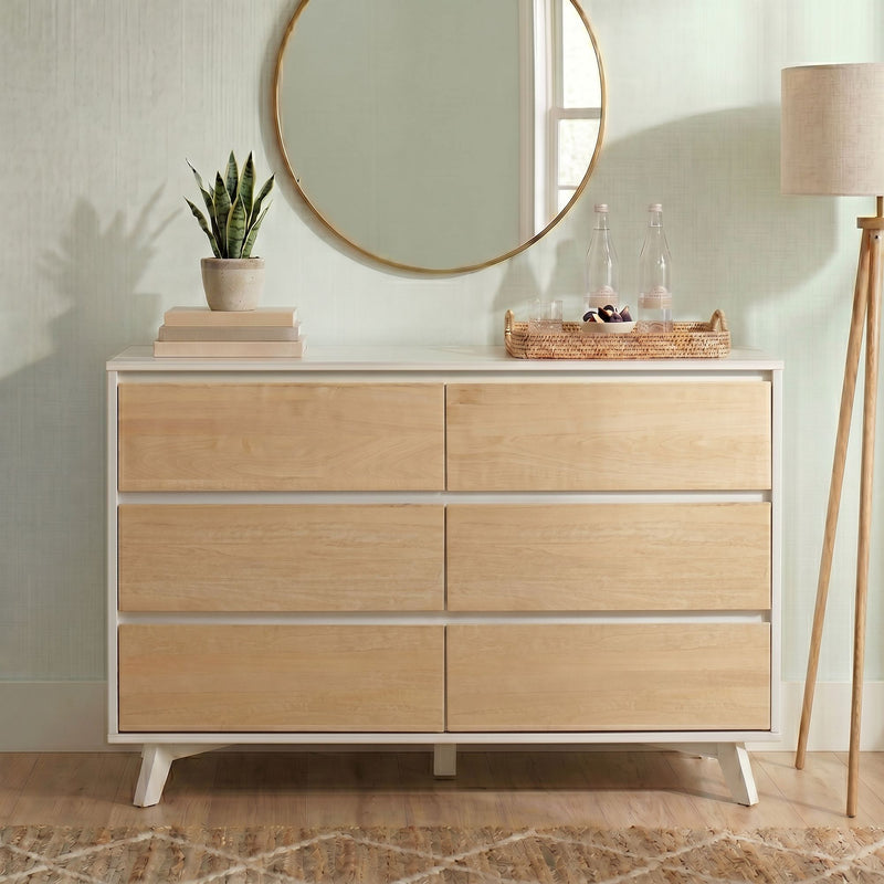 Minimalist light wood dresser with round gold mirror, snake plant on stacked books, wicker tray with glass bottles and bowl, tripod floor lamp in a modern entryway