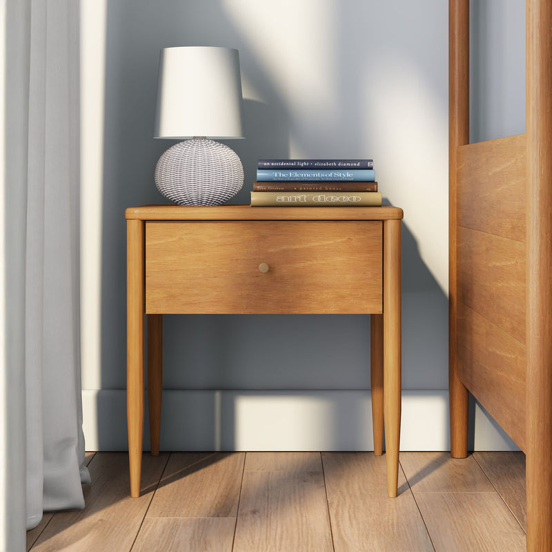 Mid-century modern wooden bedside nightstand with single drawer, white textured table lamp and stacked design books in a bright bedroom