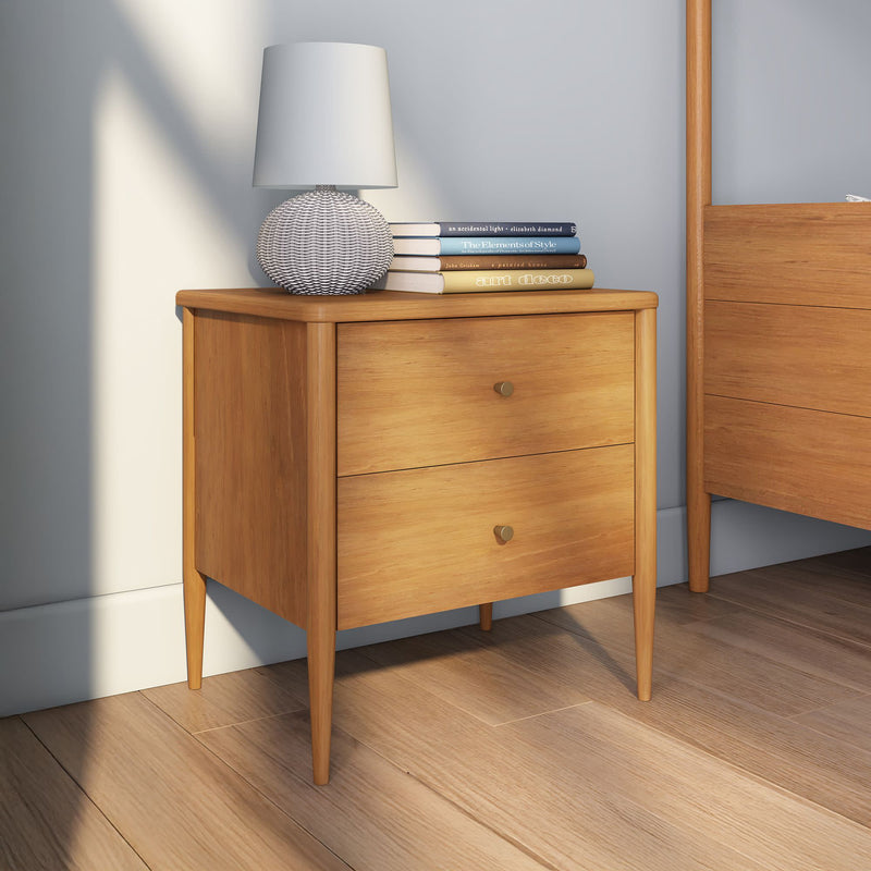 Mid-century modern two-drawer oak bedside table with tapered legs, white textured table lamp and stacked books in a bright minimalist bedroom