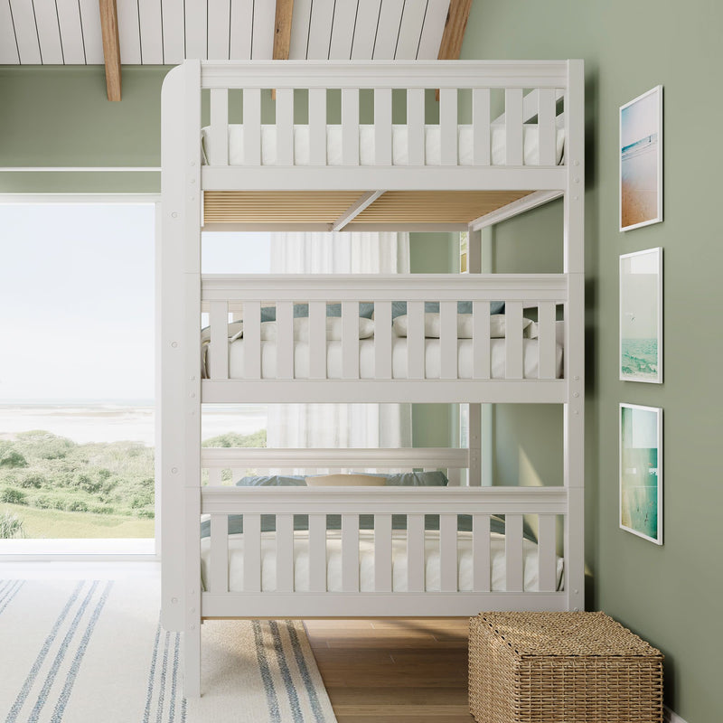 White three-tier bunk bed in coastal kids bedroom with sage green walls, beach-view window, natural light and wicker storage