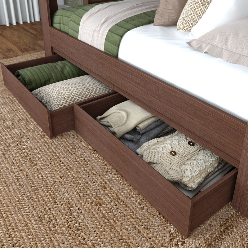 Under-bed storage drawers in walnut wood bed frame holding folded sweaters, pillows and green quilt on jute rug — bedroom organization and storage solution