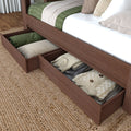 Under-bed storage drawers in walnut wood bed frame holding folded sweaters, pillows and green quilt on jute rug — bedroom organization and storage solution