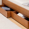 Wooden platform bed with under-bed pull-out drawers storing folded towels and blankets for space-saving bedroom storage