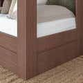 Close-up of walnut-finish four-poster platform bed corner with beige bedding, low-profile mattress and integrated storage panel on woven jute rug in a modern farmhouse bedroom