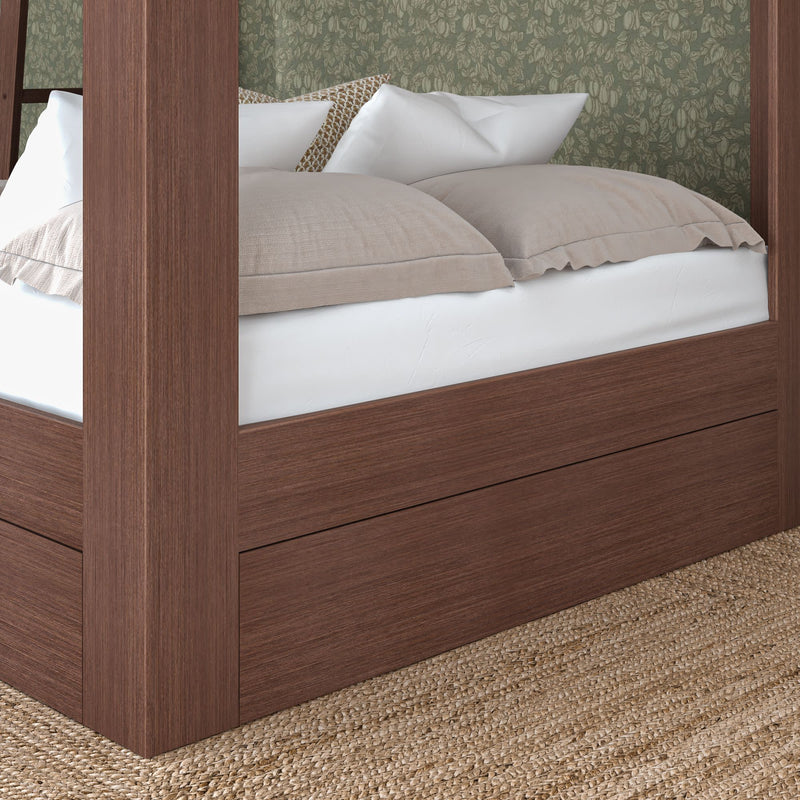 Close-up of brown wooden canopy bed frame with built-in storage drawer, white mattress and beige pillows against green floral wallpaper, woven jute rug underneath