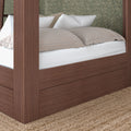 Close-up of brown wooden canopy bed frame with built-in storage drawer, white mattress and beige pillows against green floral wallpaper, woven jute rug underneath