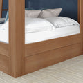 Modern oak four-poster platform bed with crisp white linens, patterned pillows and teal accent cushions on a textured beige rug