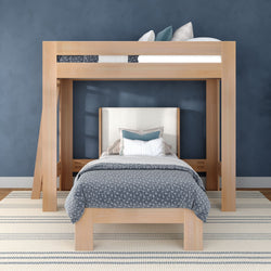 Modern light-wood loft bed with twin bed underneath, gray patterned bedding and decorative pillows against a navy blue wall on a striped rug — space-saving kids bedroom design