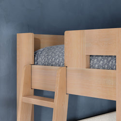 Light oak wooden bunk bed ladder and guardrail with grey patterned mattress and textured blue wall background