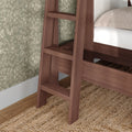 Close-up of walnut-finish wooden ladder attached to bed frame over woven jute rug with green floral wallpaper in bedroom