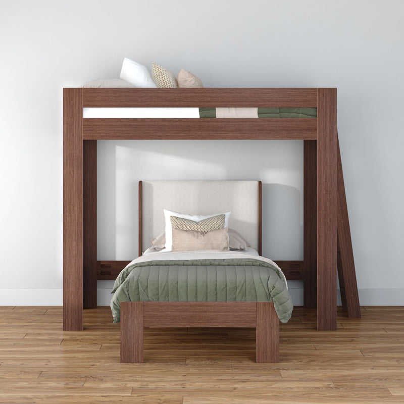 Space-saving modern wooden loft bunk bed (twin over full) with green quilted comforter, beige upholstered headboard and decorative pillows on hardwood floor in minimalist white bedroom.