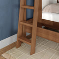 Close-up of a modern wooden bunk bed ladder in warm walnut-tone finish against a blue textured wall with a beige geometric rug and hardwood floor