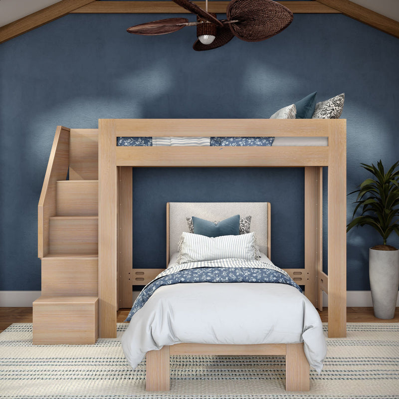Modern light-wood loft bunk bed with built-in staircase, blue-and-white striped and floral bedding, navy blue accent wall, potted plant and ceiling fan in a stylish kids' bedroom