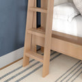 Light oak wooden ladder attached to a loft bunk bed beside a textured blue wall with white bedding and a striped beige rug in a modern bedroom