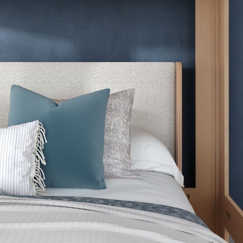 Cozy modern bedroom with navy blue accent wall, upholstered cream headboard, wooden canopy bed frame and layered white and blue decorative pillows