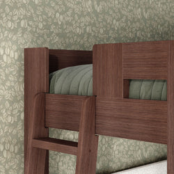 Close-up of dark wood bunk bed ladder and upper guardrail with sage-green quilted bedding against vintage floral wallpaper