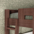 Close-up of dark wood bunk bed ladder and upper guardrail with sage-green quilted bedding against vintage floral wallpaper