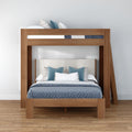 Modern wooden bunk bed frame with upholstered lower headboard, blue patterned bedding and teal and white accent pillows in a minimalist bedroom with hardwood floor and white wall