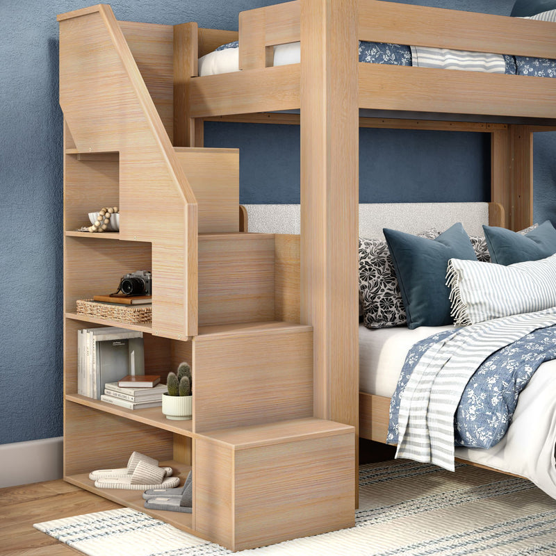 Light wood bunk bed with built-in storage stairs and open shelving, blue patterned bedding and decorative pillows in a coastal-style bedroom — space-saving kids' or guest room furniture