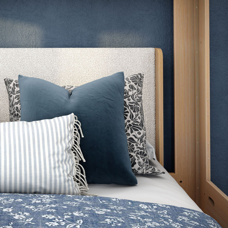 Close-up of cozy bedroom decor with navy blue decorative pillows, striped and floral accent pillows, textured cream upholstered headboard, wooden bed frame and blue floral quilt