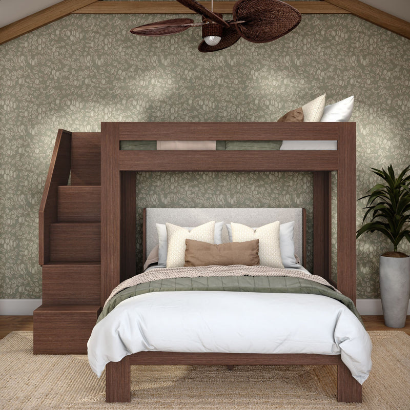 Modern wooden loft bunk bed with staircase over queen bed, neutral pillows and linens, green floral wallpaper, rattan ceiling fan and potted plant.