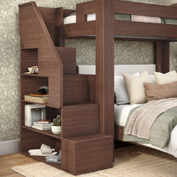 Modern dark-wood twin-over-full bunk bed with built-in staircase storage shelves, neutral green bedding and botanical wallpaper in a cozy kids' bedroom