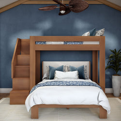 Modern wooden loft bunk bed with built-in stairs, queen-size lower bed dressed in blue floral bedding and decorative pillows against a navy accent wall with ceiling fan and potted plant
