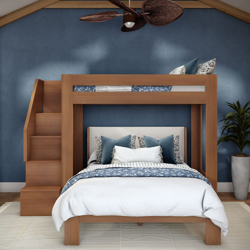 Modern wooden loft bunk bed with built-in stairs, queen-size lower bed dressed in blue floral bedding and decorative pillows against a navy accent wall with ceiling fan and potted plant