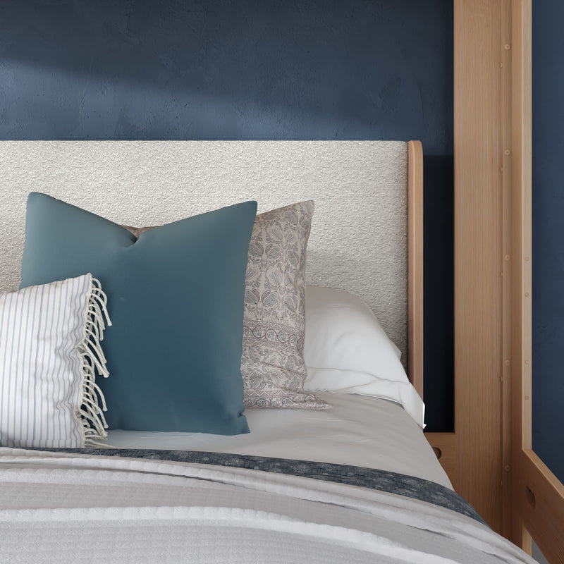 Close-up of a modern bedroom with a white textured headboard, navy accent wall, wooden bed frame and blue patterned throw pillows on white bedding