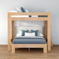 Modern natural oak bunk bed with full lower bed and twin upper bunk, upholstered headboard, blue bedding and pillows on hardwood floor