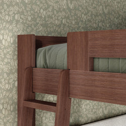 Close-up of walnut-finish solid wood bunk bed ladder and guardrail with green quilted bedding against vintage floral wallpaper